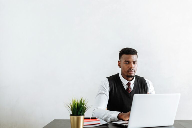 Professional man sitting at a desk working on a laptop in a modern office environment.